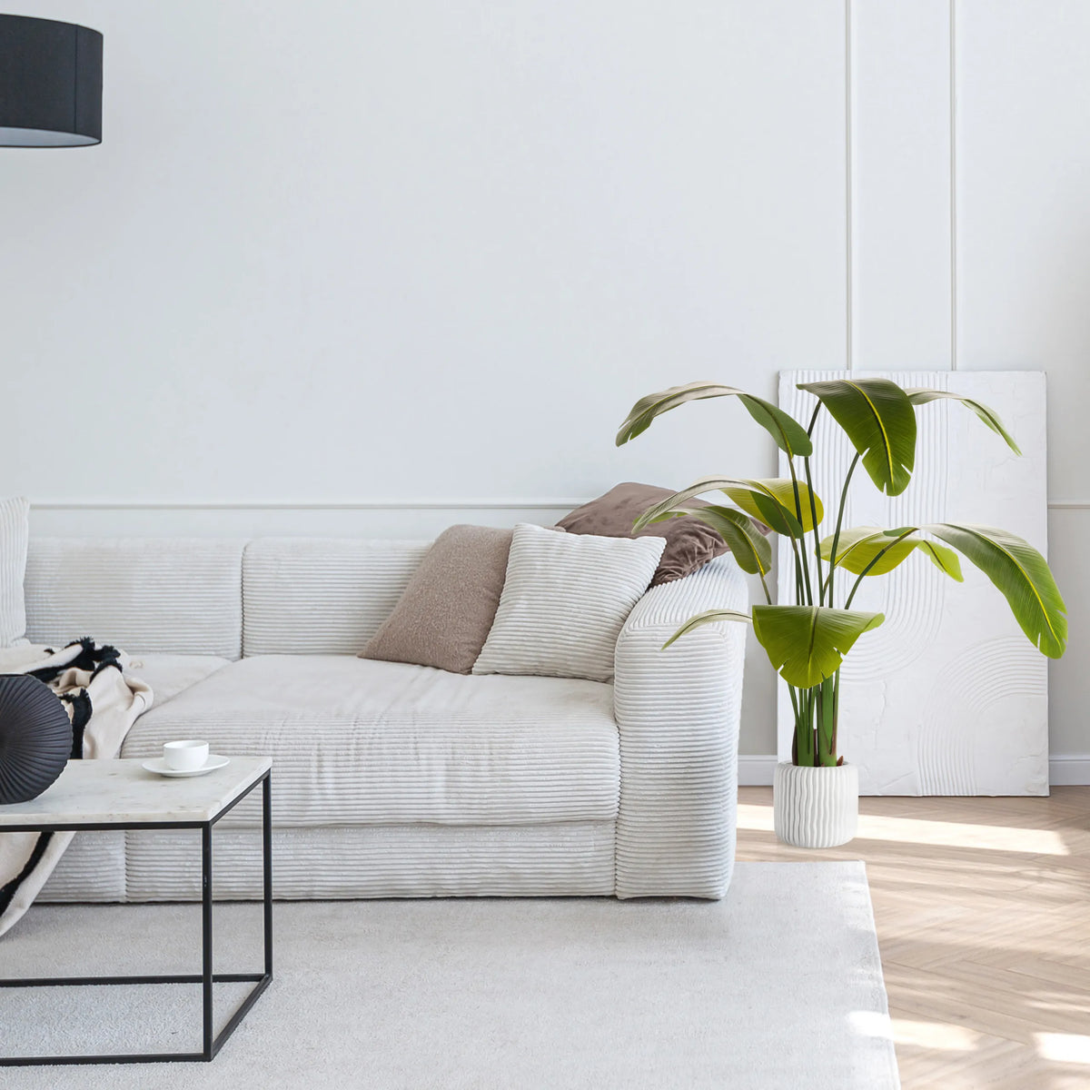 Planta artificial verde BANANE en una maceta blanca junto a un sofá de hjh OFFICE