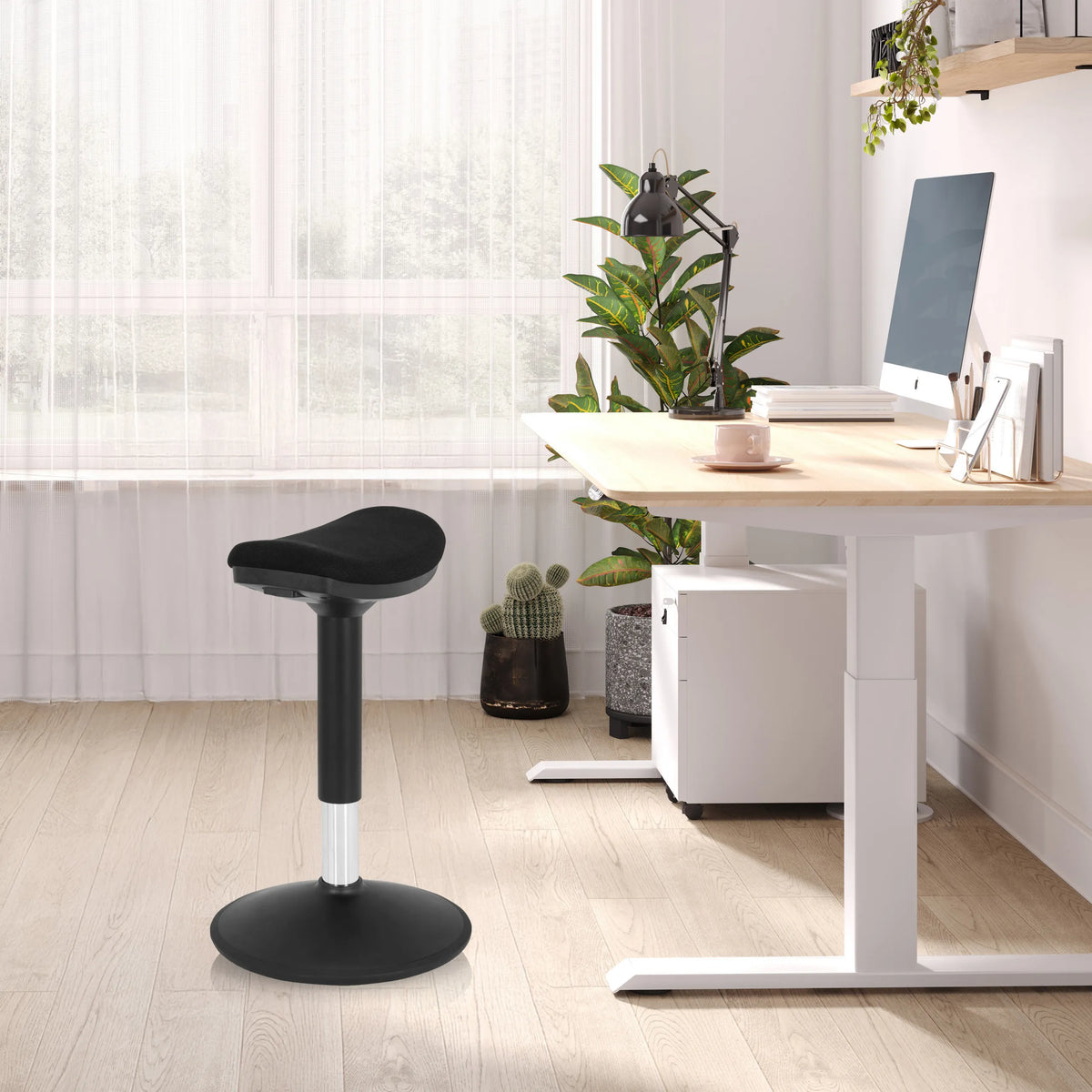 Asiento de pie BALANCE SIT I B negro con base redonda y asiento acolchado en una oficina luminosa de hjh OFFICE