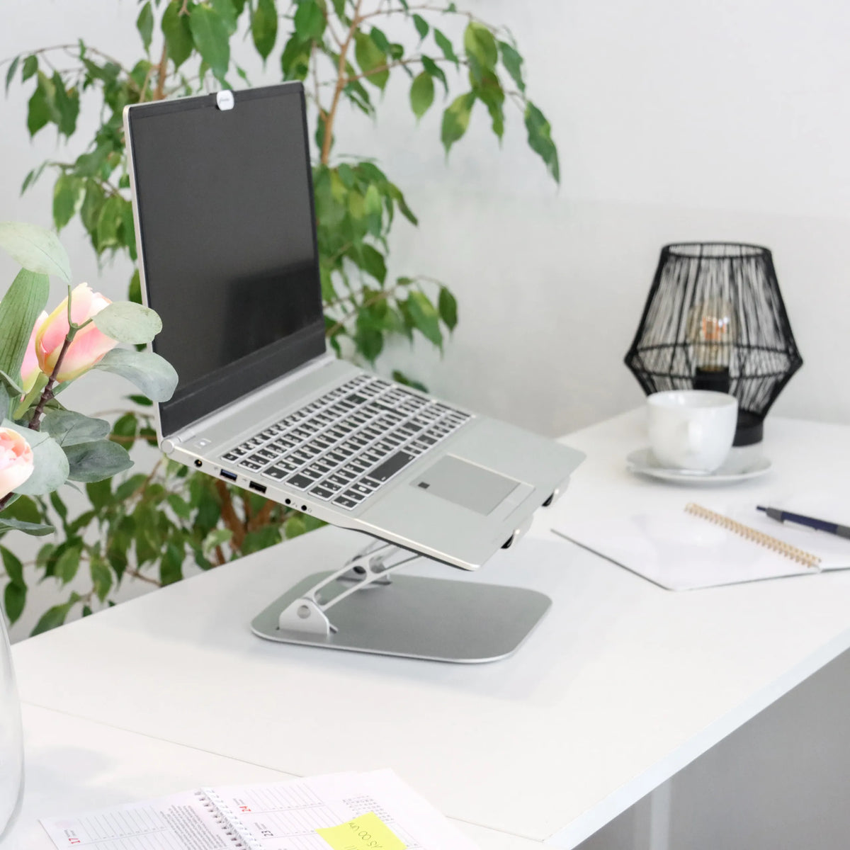 Soporte para portátil LAPTOP STAND plateado con soporte ajustable sobre un escritorio blanco de hjh OFFICE