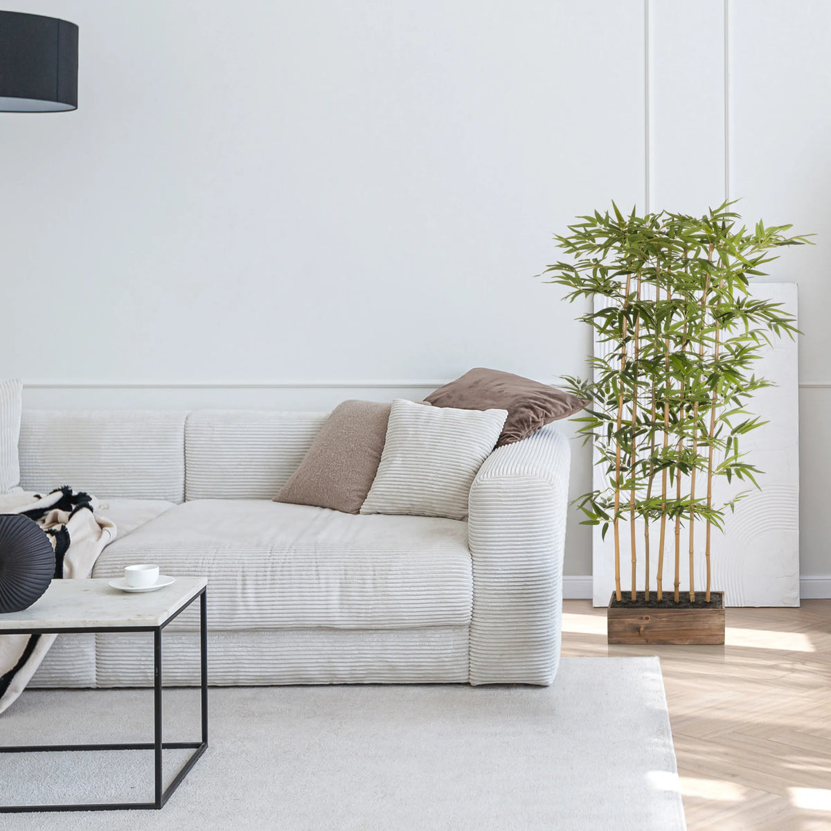 Planta artificial verde BAMBUS I en un recipiente de madera junto a un sofá blanco de hjh OFFICE