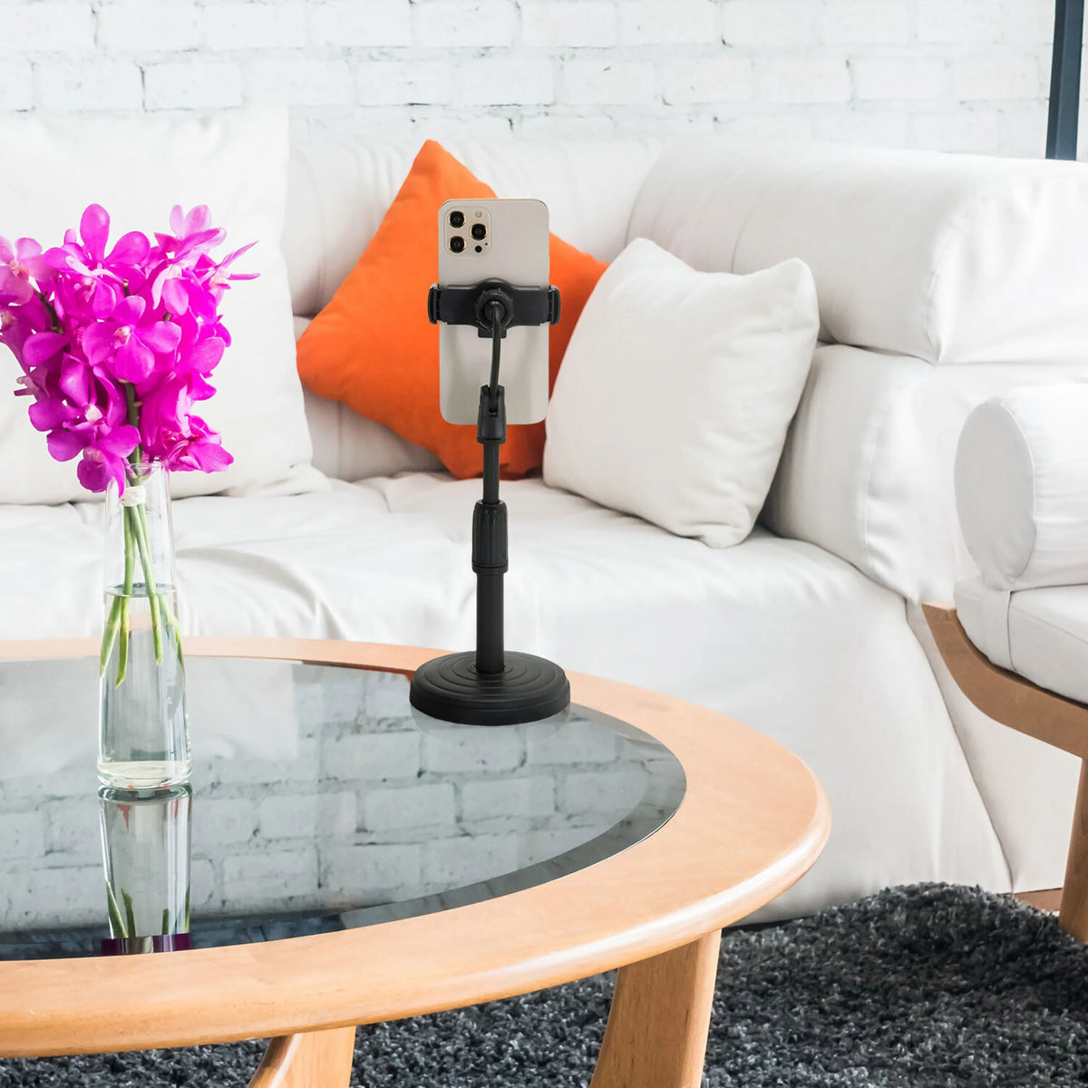 Soporte para teléfono móvil y tableta FLEXMOBI II negro con un smartphone sobre una mesa de cristal frente a un sofá blanco de hjh OFFICE