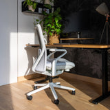 Silla alta gama VERVIO de color gris claro con ruedas y reposabrazos delante de un escritorio de hjh OFFICE
