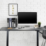 Escritorio de pie negro STAND CR con monitor, teclado y archivadores delante de una pared de ladrillo blanco de hjh OFFICE