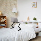 Soporte de escritorio VM-SA II negro con un portátil sobre una cama en una habitación luminosa de hjh OFFICE