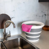 Contenedor plegable CLEAN SILR en gris y blanco con un paño rosa sobre una superficie de trabajo junto a un lavabo de hjh OFFICE