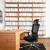Silla alta gama NOVA PRO I negra con reposacabezas y respaldo de malla delante de un escritorio de madera de hjh OFFICE