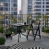 Mesa plegable TRAVANO T1 negra de 79 × 79 cm en un balcón de hjh LIVING (imagen generada por IA)