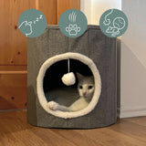 Cueva para gatos PAWY R gris con borde de piel blanca, pelota de juguete integrada y un gato en su interior de hjh LIVING