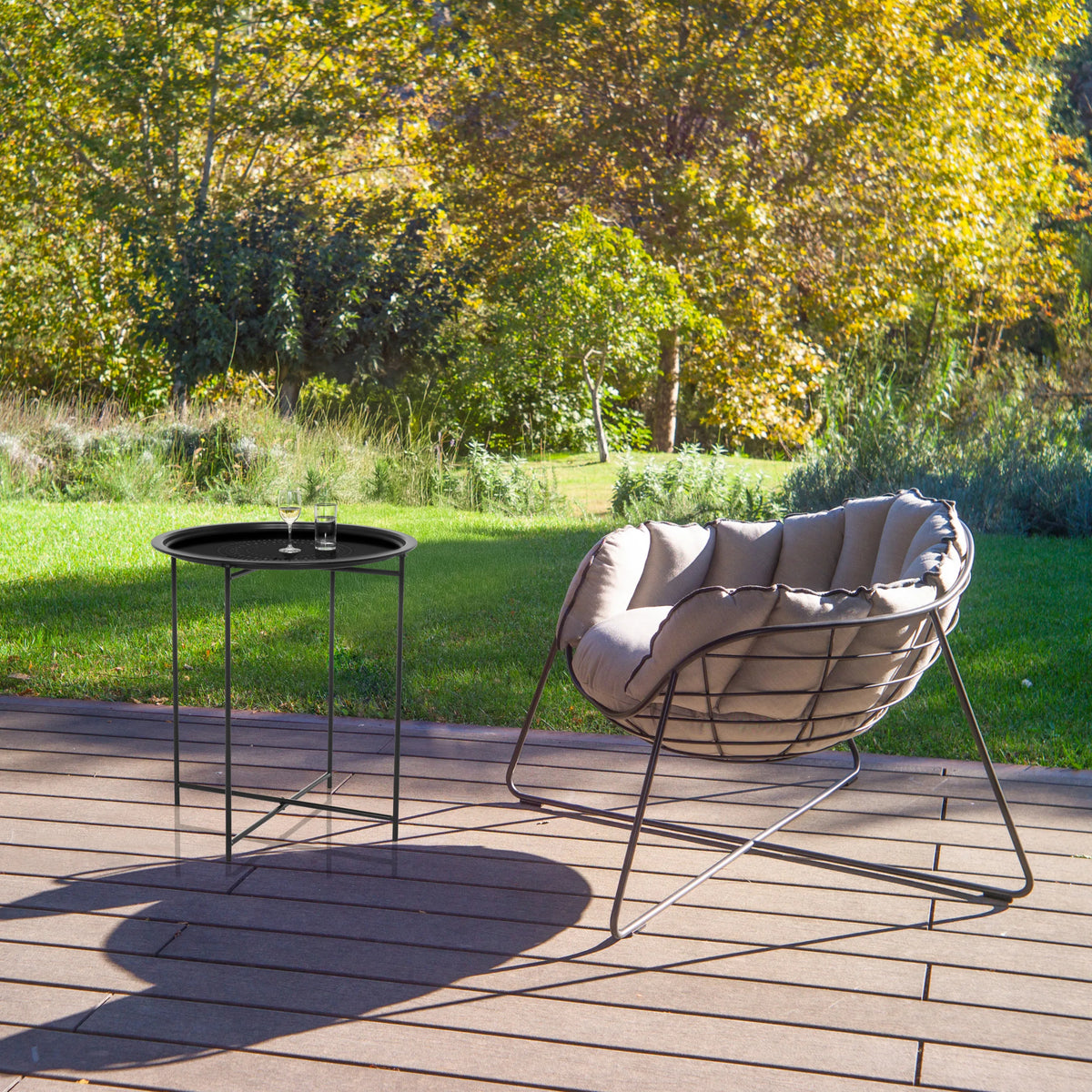 Mesa auxiliar ALLRUND de metal negro con patrón perforado en una terraza junto a un sillón de descanso de hjh LIVING