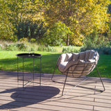 Mesa auxiliar ALLRUND de metal negro con patrón perforado en una terraza junto a un sillón de descanso de hjh LIVING